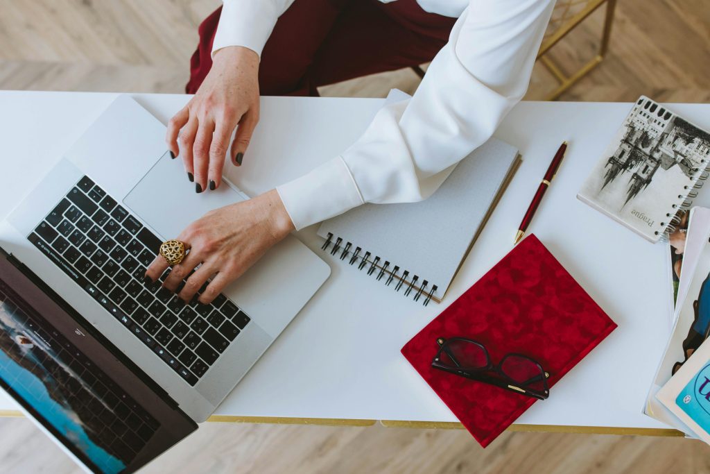 Overhead view of a workspace featuring a laptop, notepad, and eyeglasses.